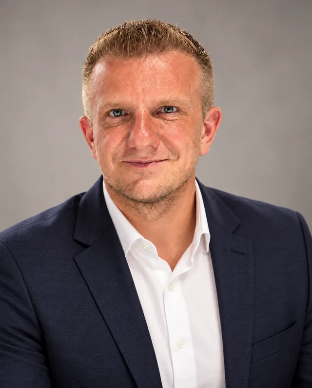 Eugen Gretz im dunkelblauen Sakko vor grauem Hintergrund